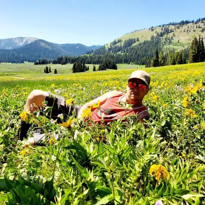 Brett lounging in a field of yellow wildflowers with mountains behind him